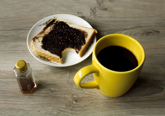 a yellow cup of coffee and saucer with bited sandwich on gray wooden table