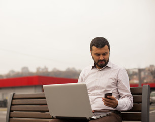 Man using phone and laptop outdoor