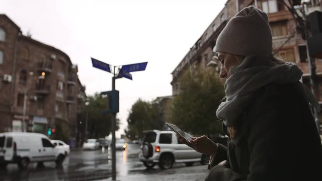 Young woman using cellphone at the street on a rainy evening in the town
