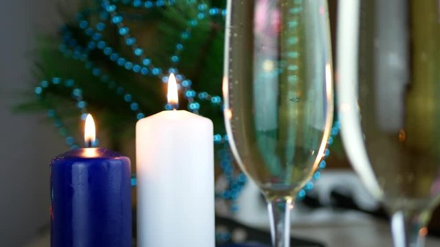 White and blue wax candles burn with sparkling wine pouring in champagne glasses closeup. Success celebrating