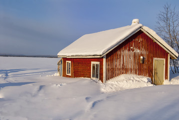 maison finlandaise rouge au bord d'un lac gelé, sous la neige