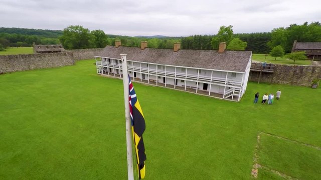 Aerial of the Calvert Arms/King&rsquo;s Colors flag waving in the breeze with the barracks in the distance at Fort Frederick in Maryland.