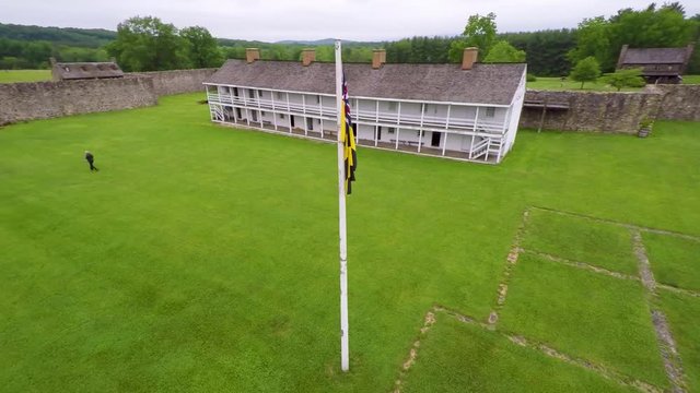 Aerial orbit around the Calvert Arms flag waving in the breeze with the barracks in the distance at Fort Frederick in Maryland.