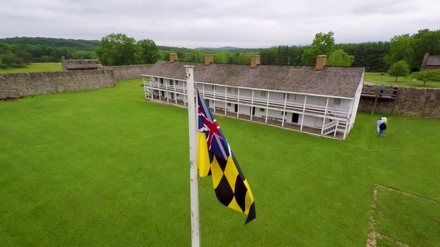 Aerial of the Calvert Arms/King&rsquo;s Colors flag waving in the breeze with the barracks in the distance at Fort Frederick in Maryland.
