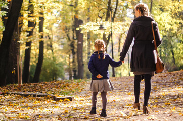 Fototapeta premium Mother with daughter walking in the park in autumn holding hands