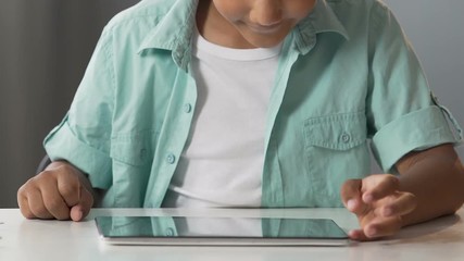 Biracial boy sitting at table with tablet, scrolling screen, modern technologies - Powered by Adobe