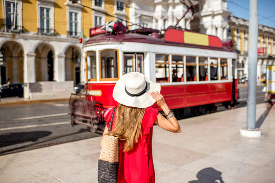 Young woman traveler standing back near the red old tourist tram on the Commerce square during the sunny weather in Lisbon city, Portugal
