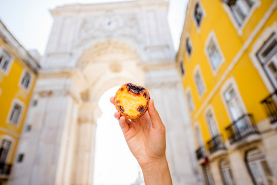 Holding portuguese egg tart pastry called pastel de Nata outdoors on the triumphal arch background in Lisbon
