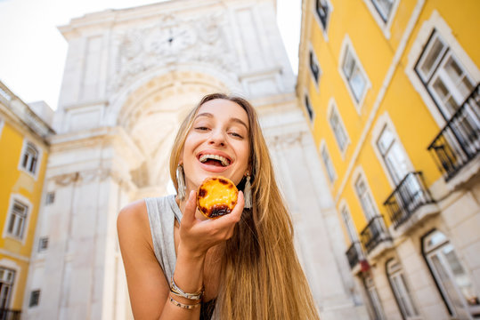 Young woman holding portuguese egg tart pastry called pastel de Nata outdoors on the triumphal arch background in Lisbon
