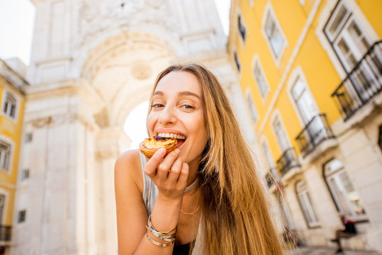 Young woman holding portuguese egg tart pastry called pastel de Nata outdoors on the triumphal arch background in Lisbon