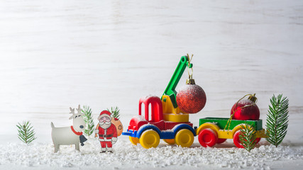 A small toy car is a crane. New Year and Christmas background. Mini Christmas trees from real spruce. Santa Claus made of paper. A blank for a postcard or a poster.