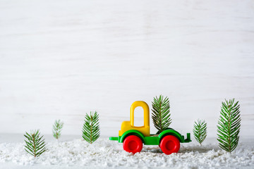 A small toy car is a crane. New Year and Christmas background. Mini Christmas trees from real spruce. Santa Claus made of paper. A blank for a postcard or a poster.