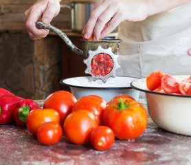 the man cook grinds pieces of ripe tomatoes into an old vintage hand-grinder for cooking homemade sauce, ketchup