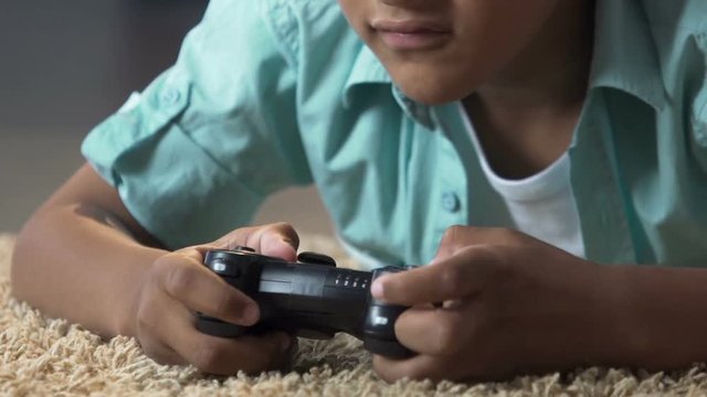 Little child lying on floor with play station control playing video games, anger