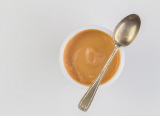 Yogurt background top view shot of caramel flavoured yoghurt in plastic cup with small silver spoon...