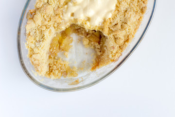 Cooked apple crumble pie in glass oval dish on white background - Top view