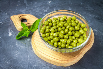 Canned peas in a wooden plate on a gray concrete background.