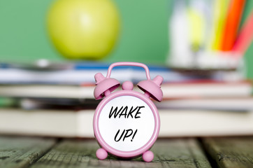 WAKE UP! message written with black on small clock with pile of books, green apple different pencils and requisites on wood isolated on green