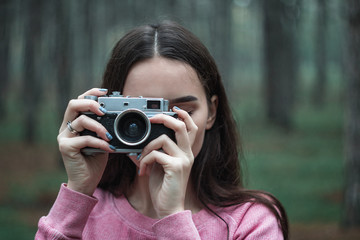 Girl photographer in the woods holds in her hand an old vintage film camera