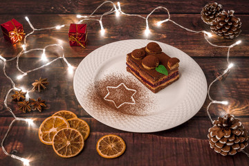 White Plate with Christmas Cake with Cinnamon, Dried Oranges, Anise, Cones, Red Gifts and Lights