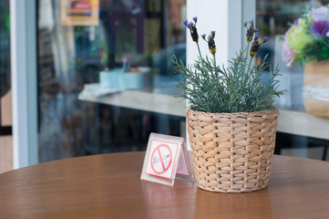 Rattan basket flower for decoration with no smoking sign on wooden table in smoking area.
