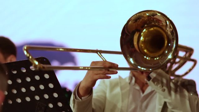 Close-up. A musician in a brass band plays solo on a trombone in white clothes.