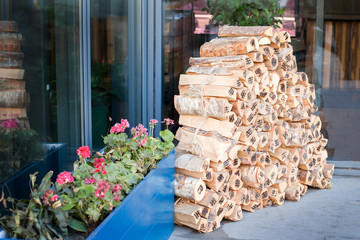 Pile of birch firewood neatly stacked near the building next to the flower bed