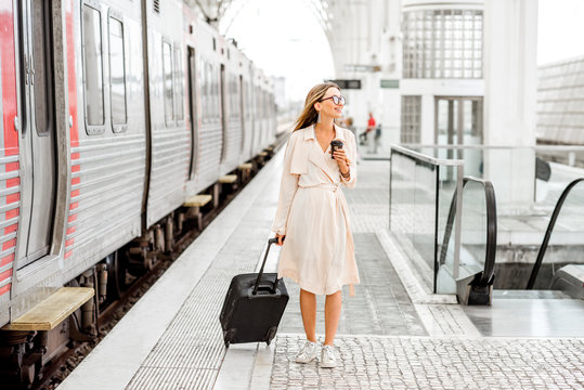 Young and beautiful woman walking with suitcase at the modern railway station near the train. Traveling by train concept
