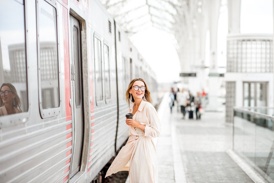 Young and beautiful woman with coffee cup boarding in the train at the modern railway station