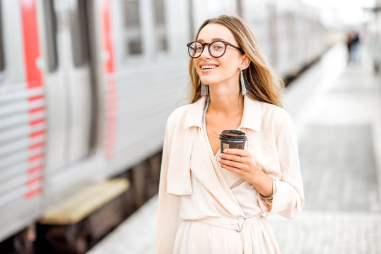 Portrait of a young elegant woman standing with coffee cup near the train at the railway station