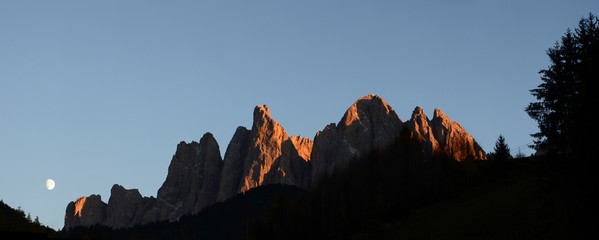 The beautiful Dolomites group of Odle at sunset with moon in the Natural Park of Odle-Puez....