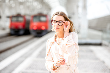 Fototapeta premium Young woman waiting for the train standing sadly on the platform at the railway station