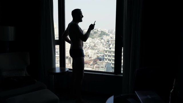 Silhouette of man texting on smartphone by window at home
