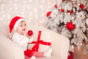 Laughing baby girl 1 year old playing with Christmas ball over Christmas background in room. Holiday season.