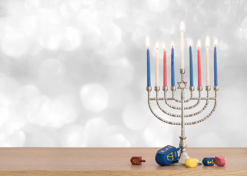 Hanukkah Jewish holiday background with menorah (Judaism candelabra)  burning candles and traditional Dreidrel game toy on wood table and on white silver winter snow bokeh