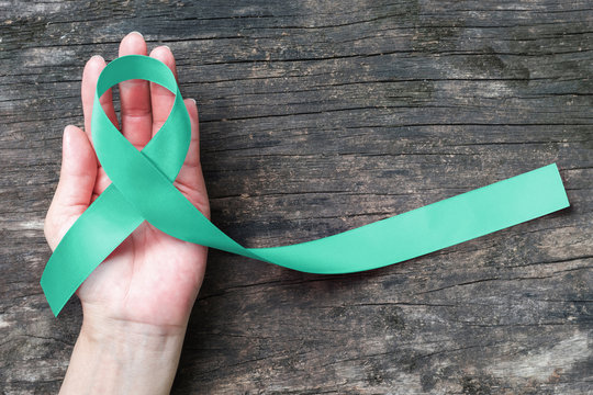 Mint green ribbon awareness for Genetic Disorder, Ivemark Syndrome, Congenital hepatic Fibrosis, and Autosomal Recessive Polycystic Kidney Disease with bow on helping hand support on aged wood