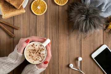 Female hands holding cup of coffee on wooden background.