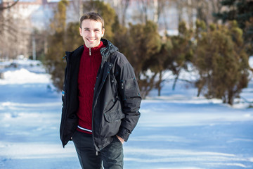 Portrait of handsome young man in red in a sunny snowy day. Winter lifestyle portrait of handsome young man walking in the snowy park