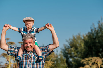 Grandfather carries grandson toddler boy on his shoulders
