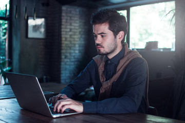 Having some emails to look through. Handsome young man using his laptop while sitting in loft interior