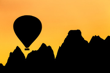 Flying hot air balloon silhouette at sunrise with rock formation in Cappadocia, Turkey