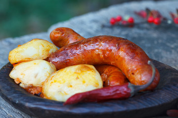 Potatoes with sausages and chilly peppers in wooden plate, rustic style