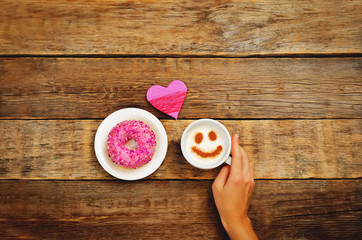 Wood background with cup of coffee, donut, heart and woman's hand