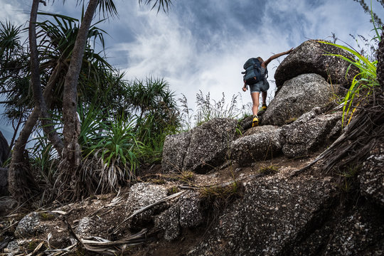 Woman hiker with backpack climbs steep rocky terrain