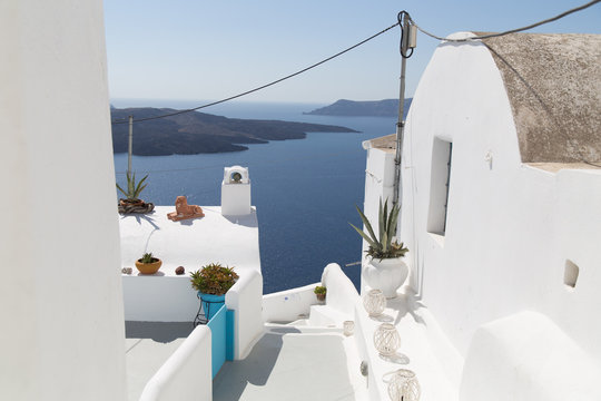 A balcony with plants in jugs and a view on a sea, mountains and city with white houses