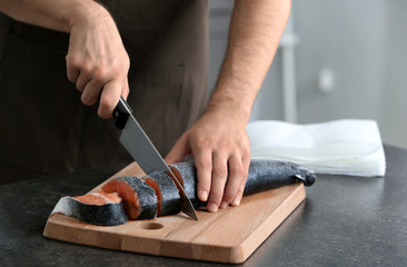 Man cutting fresh salmon in kitchen
