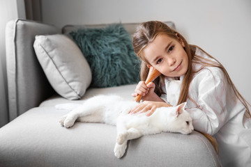 Little girl in doctor coat and white cat  on sofa indoors
