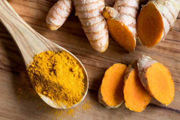 Turmeric powder on a wooden spoon, with turmeric root in the background