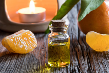 A bottle of tangerine essential oil with tangerines and an aroma lamp