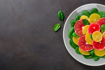 Salad made of orange and grapefruit slices and spinach leaves on a gray plate on dark stone background. Top view, copy space for your text, horizontal image